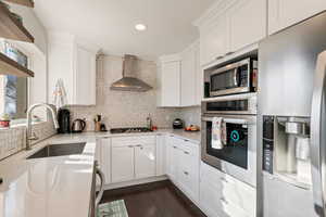 Kitchen featuring a sink, stainless steel appliances, white cabinetry, wall chimney exhaust hood, and backsplash