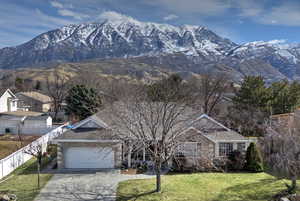 View of front of house with a mountain view, concrete driveway, a front yard, and fence