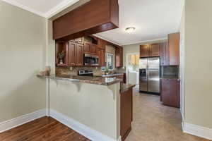 Kitchen with ornamental molding, a kitchen breakfast bar, appliances with stainless steel finishes, a peninsula, and washer / dryer