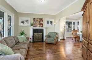 Living room with a tiled fireplace, ornamental molding, arched walkways, and wood finished floors