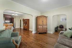 Living room with a notable chandelier, arched walkways, crown molding, baseboards, and dark wood-style flooring