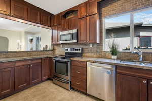 Kitchen featuring light tile patterned floors, decorative backsplash, stainless steel appliances, and a sink