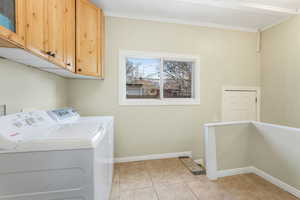 Washroom featuring baseboards, washing machine and dryer, ample light, ornamental molding, light tile  and cabinet space