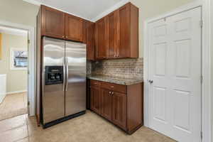 Kitchen with baseboards, dark stone counters,  tile flooring, and stainless steel fridge