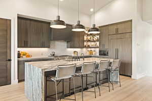 Kitchen with wall chimney exhaust hood, modern cabinets, paneled fridge, a breakfast bar, and decorative backsplash