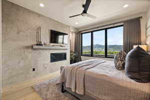 Bedroom with wood finished floors, a glass covered fireplace, recessed lighting, and a ceiling fan