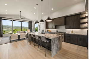 Kitchen featuring high end stainless steel range oven, open shelves, wall chimney exhaust hood, a ceiling fan, and a kitchen breakfast bar