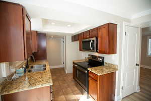 Kitchen featuring light granite counters, a sink, ornamental molding, stainless steel appliances, and a raised ceiling