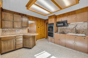 Kitchen featuring a sink, black appliances, wood walls, and light countertops