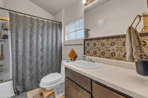 Full bath with tile patterned floors, toilet, shower / bath combo, vanity, and vaulted ceiling