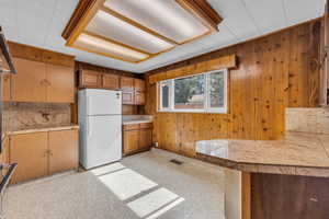 Kitchen with visible vents, freestanding refrigerator, tile countertops, wood walls, and brown cabinetry