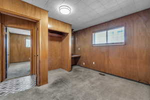 Unfurnished bedroom featuring visible vents, carpet, a closet, and wood walls