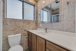 Bathroom featuring vanity, tile walls, toilet, and an enclosed shower