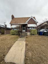 Bungalow-style home featuring brick siding, a chimney, a front lawn, and fence