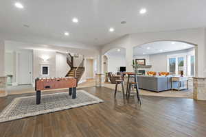 Playroom with wood finished floors, a fireplace, arched walkways, recessed lighting, and baseboards