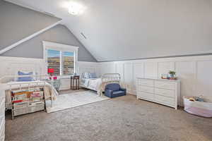 Bedroom with a decorative wall, carpet, vaulted ceiling, and a wainscoted wall