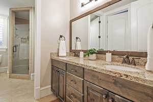 Bathroom featuring a stall shower, double vanity, and baseboards
