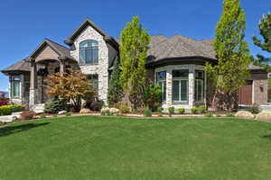 French country inspired facade with a garage, stone siding, a front yard, and a shingled roof
