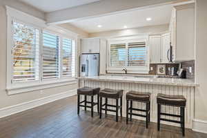 Kitchen featuring appliances with stainless steel finishes, light stone countertops, a peninsula, dark wood-style floors, and tasteful backsplash