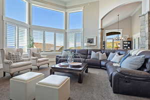 Carpeted living room featuring a chandelier, arched walkways, ornamental molding, and high vaulted ceiling