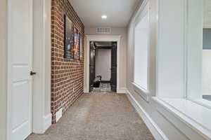 Hall featuring brick wall, carpet floors, and baseboards