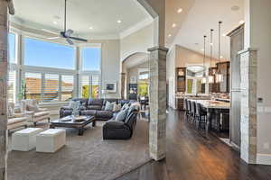 Living room with ornate columns, a ceiling fan, arched walkways, dark wood-style flooring, and ornamental molding