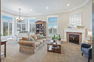 Carpeted living room featuring healthy amount of natural light, a brick fireplace, ornamental molding, a chandelier, and recessed lighting