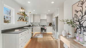 Kitchen with a sink, appliances with stainless steel finishes, white cabinetry, dark countertops, and backsplash