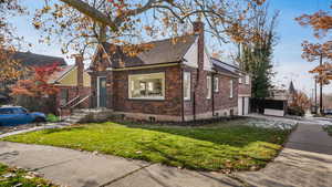 View of front of home with a front yard, driveway, a chimney, a garage, and brick siding