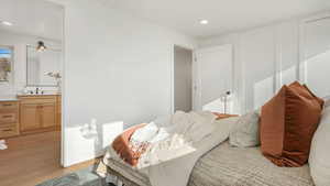 Bedroom with a sink, light wood-type flooring, ensuite bathroom, and recessed lighting