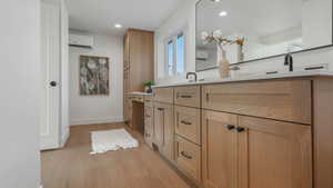 Bathroom featuring baseboards, an AC wall unit, recessed lighting, wood finished floors, and vanity