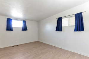 Unfurnished room featuring a textured ceiling, wood finished floors, visible vents, and baseboards