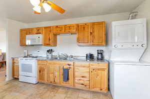 Kitchen featuring a sink, white appliances, ceiling fan, and stacked washing maching and dryer