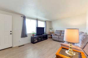 Living area with visible vents, a textured ceiling, baseboards, and light wood-style floors