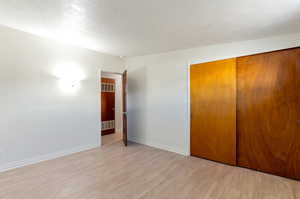 Unfurnished bedroom with light wood-style floors, visible vents, a textured ceiling, a closet, and baseboards