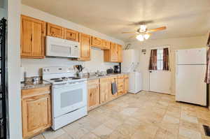 Kitchen featuring white appliances, a ceiling fan, a sink, light countertops, and stacked washer and clothes dryer