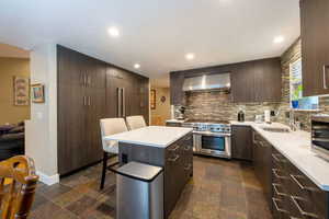 Kitchen with a sink, high end stainless steel range oven, wall chimney exhaust hood, and stone tile flooring