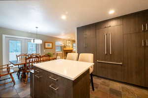 Kitchen with a center island, decorative light fixtures, a kitchen bar, light countertops, and stone tile flooring