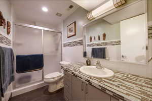 Bathroom with visible vents, a shower stall, tile walls, toilet, and vanity