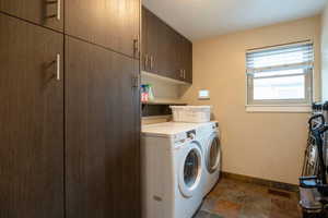 Washroom featuring washer and dryer, baseboards, cabinet space, and stone finish flooring