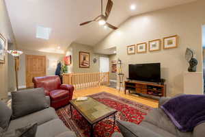 Living room featuring recessed lighting, vaulted ceiling with skylight, a ceiling fan, and wood finished floors