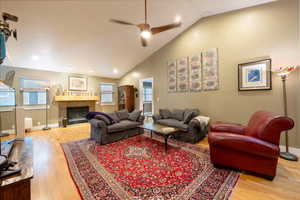 Living room featuring high vaulted ceiling, a ceiling fan, a tiled fireplace, wood finished floors, and baseboards