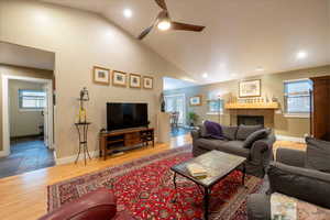 Living room with baseboards, ceiling fan, a tile fireplace, wood finished floors, and high vaulted ceiling