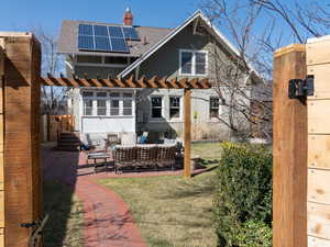 Rear view of property featuring solar panels, a shingled roof, a chimney, a patio area, and a pergola