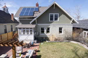 Rear view of house featuring solar panels, a patio area, a lawn, and a shingled roof