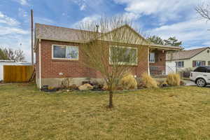View of front of home with brick siding, roof with shingles, a front yard, and fence