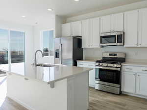 Kitchen with appliances with stainless steel finishes, a sink, a kitchen island with sink, white cabinets, and recessed lighting