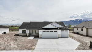 View of front of home featuring roof with shingles, an attached garage, stone siding, a mountain view, and driveway