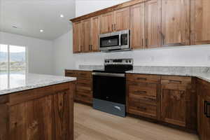 Kitchen featuring visible vents, light stone counters, lofted ceiling, light wood-style floors, and stainless steel appliances