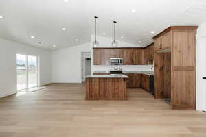 Kitchen with a kitchen island, appliances with stainless steel finishes, open floor plan, light wood-style floors, and lofted ceiling